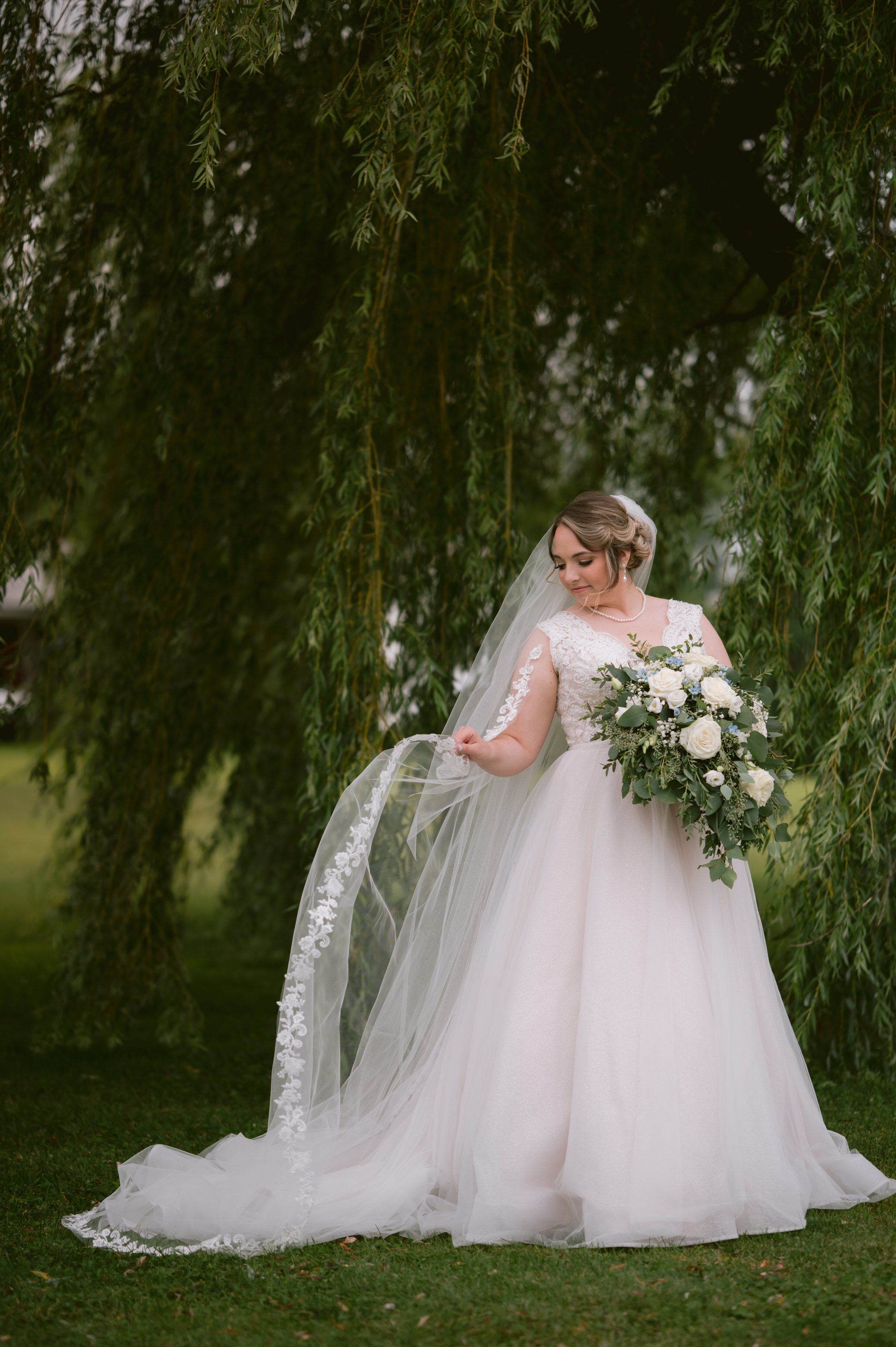 Bride holding her bouquet beneath a willow tree